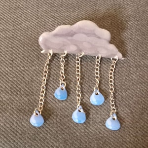 May include: A grey cloud charm with five silver chains and blue raindrop charms hanging from it.