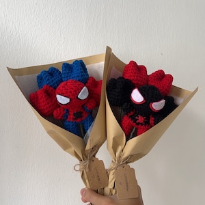 May include: Two crocheted bouquets of red and blue roses with a Spiderman character in the center. Each bouquet is wrapped in brown paper and tied with twine. A brown tag with the text "CHIVGARDEN" is attached to each bouquet.