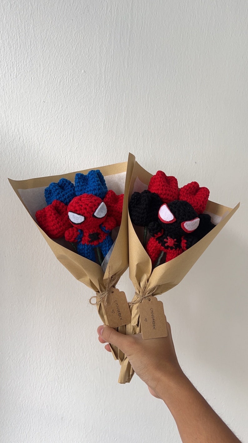 May include: Two crocheted bouquets of red and blue roses with a Spiderman character in the center. Each bouquet is wrapped in brown paper and tied with twine. A brown tag with the text "CHIVGARDEN" is attached to each bouquet.