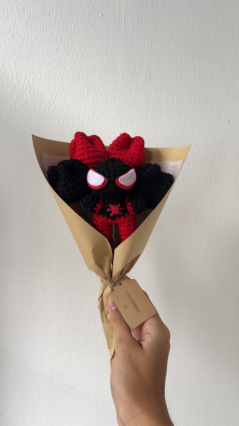 May include: A crocheted red and black Spider-Man character in a brown paper bouquet with a tag that says "CHIVY GARDEN" with a heart symbol.