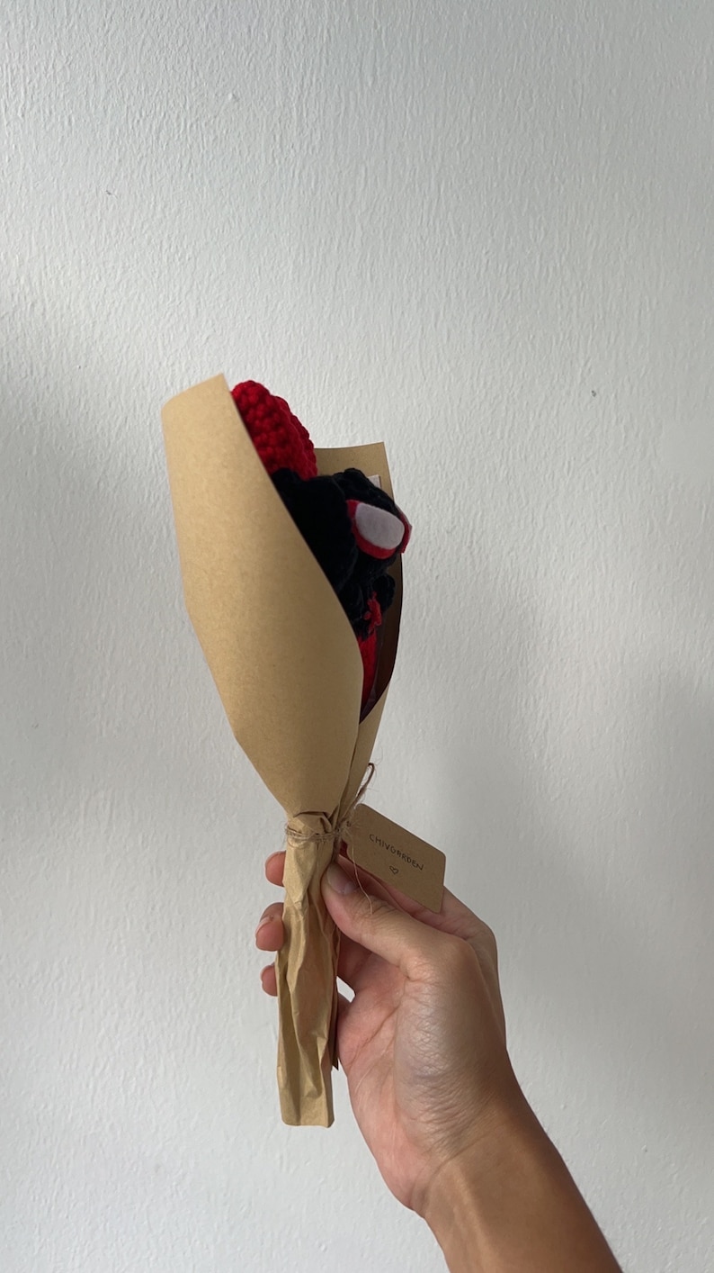 May include: A small bouquet of crocheted flowers in red and black, wrapped in brown paper with a tag that says "CHINO GARDEN".