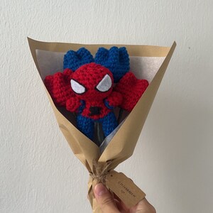 May include: A brown paper bouquet with a crocheted Spiderman figure in the center. The bouquet is tied with twine and has a small brown tag that says "CHIVARDEEN" with a heart symbol.
