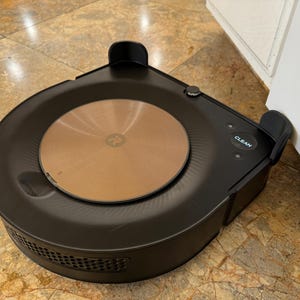 May include: A black robotic vacuum cleaner with a round, brown dustbin and a "CLEAN" button on the side.