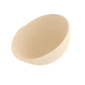May include: A beige, oval-shaped woven basket with a spiral design at the base. The basket is made of tightly coiled rope, creating a textured surface. The interior is a lighter shade of beige.