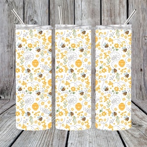 May include: Three stainless steel tumblers with a white background and a pattern of yellow bees, flowers, and honeycomb. The tumblers have a straw in each.