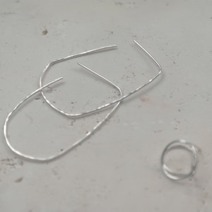 May include: Two silver hoop earrings and a silver ring. The earrings are in the shape of a rectangle with rounded corners. The ring is a simple band.