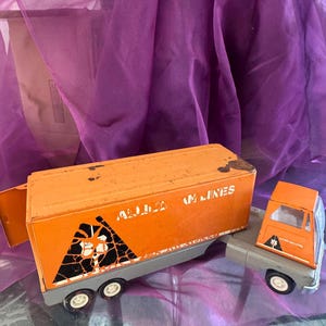 May include: Orange toy semi-truck with a trailer. The trailer has the words "Atlanta Air Lines" printed on the side. The truck has a black and white graphic of a mountain on the side.