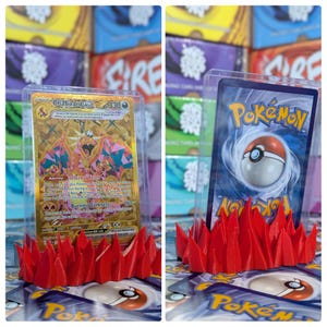 May include: A red plastic Pokemon card display stand with a clear plastic case holding a Charizard GX Pokemon card. The card features a gold and pink design with the text "Charizard GX" and "Internal Flame".