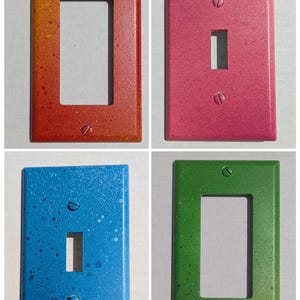 May include: Four colorful, hand-painted light switch covers. The covers are painted in shades of red, pink, blue, and green with a speckled design. Each cover has a different style of opening for the light switch and is secured with two screws.