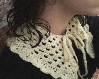 May include: A white crocheted collar with a tied bow in the front. The collar is worn over a black shirt.