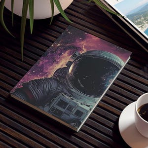 May include: A notebook with an astronaut in space design, a travel magazine, and a cup of coffee on a dark wooden table. The notebook features a space scene with an astronaut's helmet. The magazine has a landscape photo on the cover.