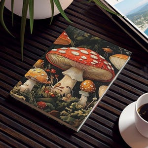 May include: A notebook with a mushroom illustration featuring red and white spotted caps, resting on a dark wooden table. A travel magazine and a cup of coffee are also on the table, with a potted plant in the background.