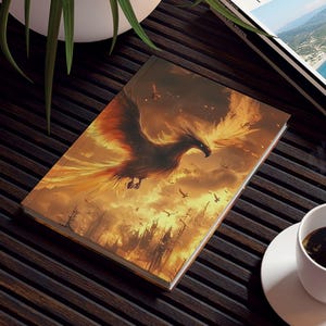 May include: A coffee table with a book featuring a phoenix illustration, a travel magazine, a white coffee cup, and a potted plant. The book cover displays a fiery phoenix rising against a cloudy sky.