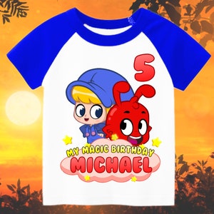May include: White t-shirt with blue sleeves featuring a cartoon character with a red creature. The shirt has the text "My Magic Birthday Michael" and the number "5" on it.