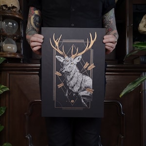 Könnte beinhalten: Ein Schwarzweißdruck eines Hirsches mit zwei Köpfen, umgeben von goldenen Pfeilen und geometrischen Formen. Der Druck ist auf schwarzem Papier und hat einen goldenen Rand.