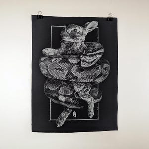 Könnte beinhalten: Schwarz-Weiß-Kunstdruck mit einem Kaninchen, das von einer Schlange umschlungen wird. Das Kaninchen befindet sich in der Mitte, die Schlange windet sich darum. Das Kunstwerk ist vor einem schwarzen Hintergrund.