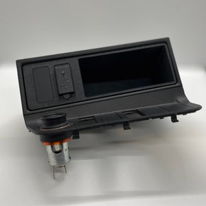 May include: Black plastic car accessory with a USB port, a cigarette lighter socket, and a small storage compartment.