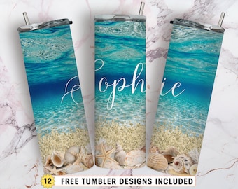 Peut inclure: Trois gobelets en acier inoxydable avec un motif de plage. Les gobelets présentent une mer bleue avec des vagues blanches, une plage de sable et des coquillages. Le gobelet du milieu porte le nom "Sophie" écrit en cursive blanche.