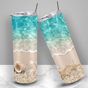 May include: Two stainless steel insulated tumblers with lids and straws. The tumblers feature a beach scene with turquoise water, white waves, sand, seashells, starfish, and glitter.