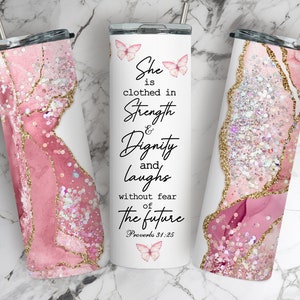 May include: A pink and gold tumbler with a glitter finish and a quote about strength and dignity. The quote reads "She is clothed in strength and dignity and laughs without fear of the future. Proverbs 31:25".
