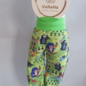 Könnte beinhalten: Grüne Hose mit einem Muster von Maulwürfen, die im Garten arbeiten. Die Hose hat einen grünen Gummizug an der Taille und am Beinabschluss. Der Text "VaReHa Die Naht zum Verlieben" befindet sich auf einem Holzschild.