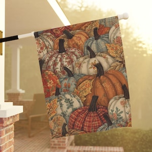 May include: A rectangular garden flag featuring a repeating pattern of pumpkins in various colors including orange, blue, and white. The pumpkins are decorated with floral, plaid, and leaf motifs, and the flag is mounted on a white pole.