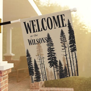 May include: A welcome sign with a beige background and black text that reads "WELCOME at the WILSONS". The sign features a silhouette of a forest with tall pine trees.
