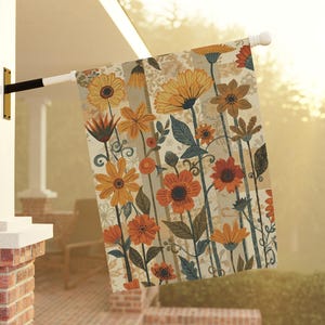 May include: A rectangular garden flag featuring a repeating pattern of stylized flowers in shades of orange, yellow, and brown against a cream-colored background with vertical stripes and subtle floral line art details throughout the design.