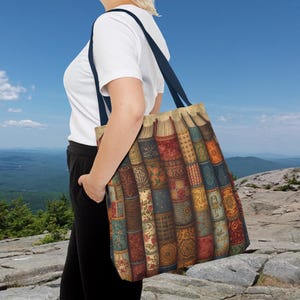 May include: A beige tote bag featuring a colorful, vintage book design. The bag has dark blue straps and is carried over the shoulder. The books have intricate patterns in shades of red, blue, and gold.