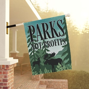 May include: A teal and green outdoor flag with the text "PARKS NOT PROFITS." The flag features a forest scene with silhouettes of a deer and a moose. The flag is hanging on a white pole.