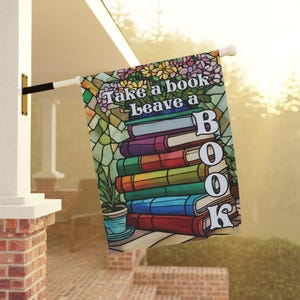 May include: A decorative flag with the text "Take a book, Leave a book" in white letters. The flag features a stack of colorful books and a floral design, creating a stained-glass effect. A small potted plant is also visible.