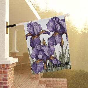May include: A white garden flag with a purple and yellow iris flower design. The flag has the text "Henderson" printed on it.