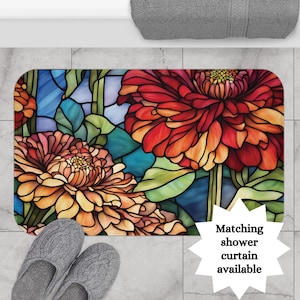 May include: A stained glass style bath mat with a floral design featuring red, orange, and yellow flowers on a blue background. The text "Matching shower curtain available" is in the lower right corner.