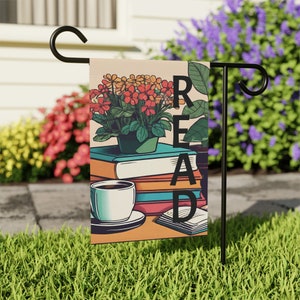 May include: A garden flag with a stack of books, a cup of coffee, and a potted plant with red and orange flowers. The word "READ" is spelled vertically on the flag.