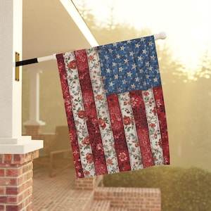 May include: A decorative American flag with a unique floral design. The flag features red and white stripes with a floral pattern, and a blue field with white stars. The flag is hanging outside a brick building.