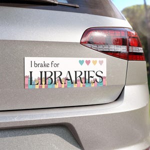 May include: A white car bumper sticker with the text "I brake for LIBRARIES" in black text. The sticker features a row of colorful books and four small hearts in pink, yellow, and blue.