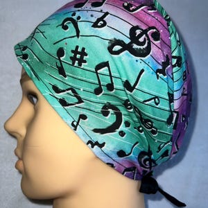 May include: A turquoise, pink and purple surgical scrub hat with a black and white musical note pattern. The hat has a black tie.