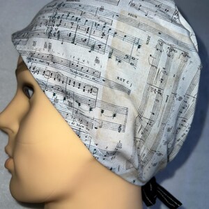 May include: A white scrub hat with a black tie. The hat is printed with a sheet music design. The music is printed in black and white. The text "KEY C" is visible on the hat.