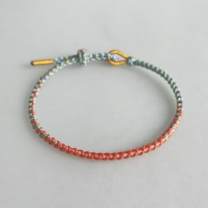Op de afbeelding: Een gevlochten armband met een blauwe, groene en oranje kleurstelling. De armband heeft een gouden sluiting.