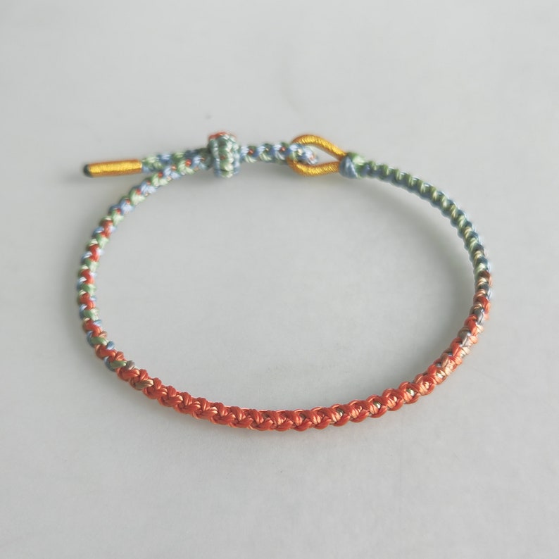 Op de afbeelding: Een gevlochten armband met een blauwe, groene en oranje kleurstelling. De armband heeft een gouden sluiting.