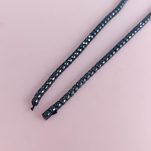 May include: A black tennis chain necklace with a clasp closure. The chain is made of small, round black stones.
