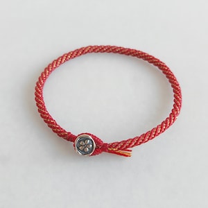 May include: Red string bracelet with a silver charm featuring a flower design.