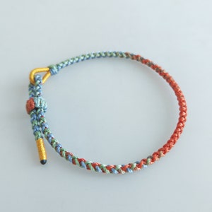 Op de afbeelding: Een gevlochten armband met een mix van blauwe, groene en oranje draden. De armband heeft een gouden sluiting.