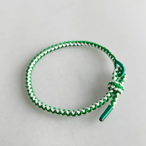 May include: A green and white braided bracelet with a knot at the end.