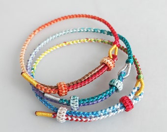 May include: Three colorful braided bracelets with knotted accents. The bracelets are made of red, orange, yellow, green, blue, and white thread.