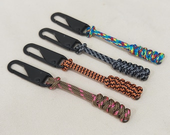 Puede incluir: Cuatro llaveros con clips metálicos negros y extremos de cuerda trenzada de colores. Las cuerdas son naranja y negra, naranja y blanca, gris y negra, y azul, roja, amarilla y verde.