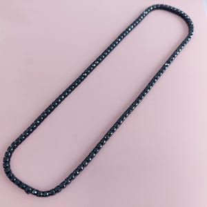 May include: A black tennis chain necklace with a classic design. The chain is made of small, round black stones.