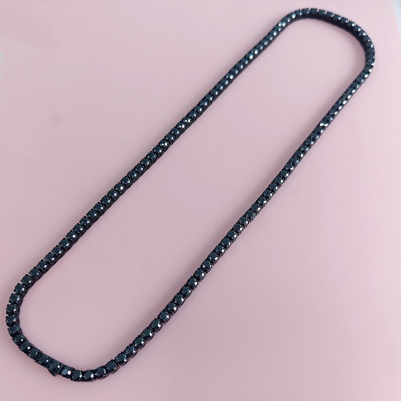 May include: A black tennis chain necklace with a classic design. The chain is made of small, round black stones.