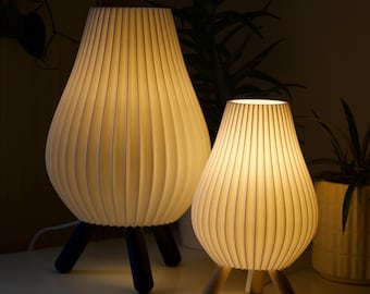 May include: Two white table lamps with pleated shades and wooden legs. The larger lamp has dark blue legs, while the smaller lamp has natural wood legs.