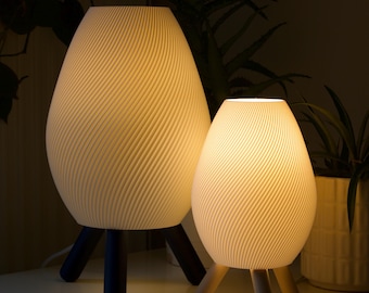 May include: Two white table lamps with a wavy, textured design. The larger lamp has black legs and the smaller lamp has wooden legs.